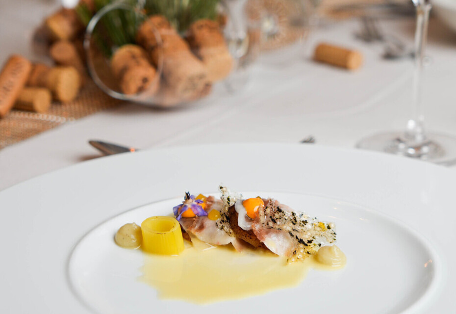 Gourmet dish elegantly presented on a white plate, set on a dining table with wine glasses and a candle in the background.