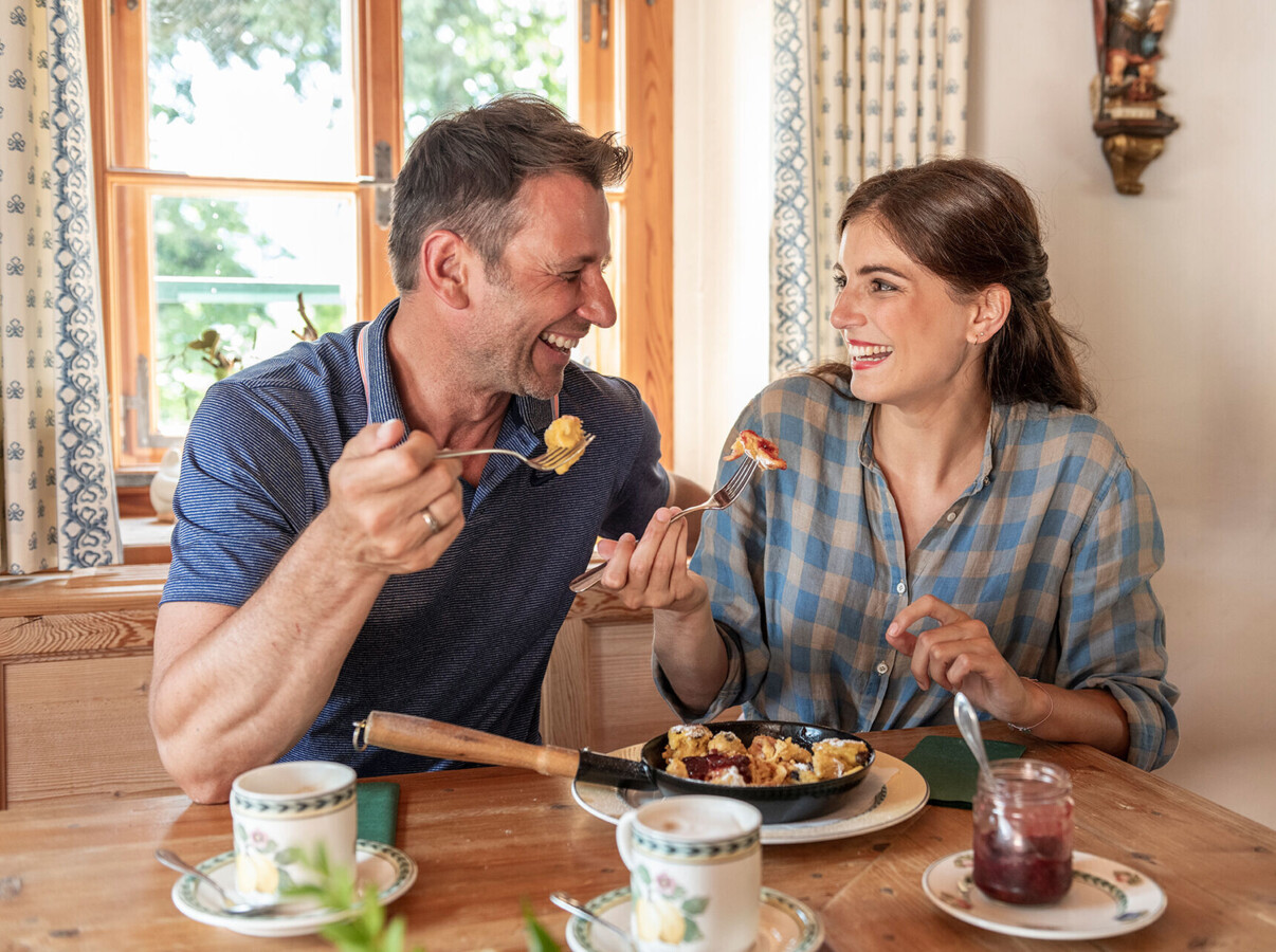 A couple enjoying a meal together at a cozy wooden table with a window view.