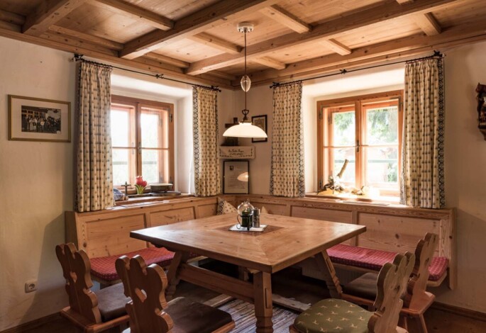 Cozy wooden dining room with patterned curtains and a central table, illuminated by natural light from two windows.