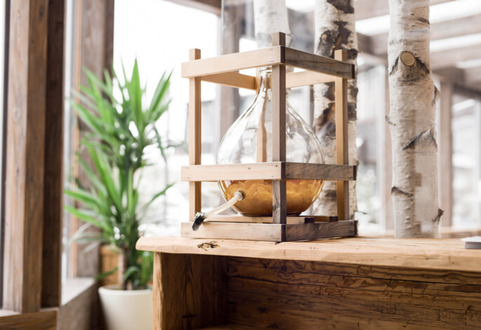 A glass vessel in a wooden frame on a rustic table, surrounded by birch trees and a green plant, in a bright, natural setting.