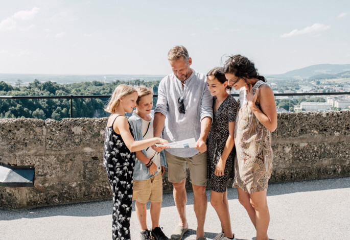 Family exploring a city map on a sunny day, with hills in the background.