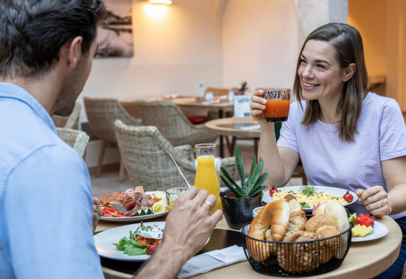 Zwei Personen genießen ein Frühstück mit frischen Säften, Gebäck und Omelett in einem gemütlichen Restaurant.