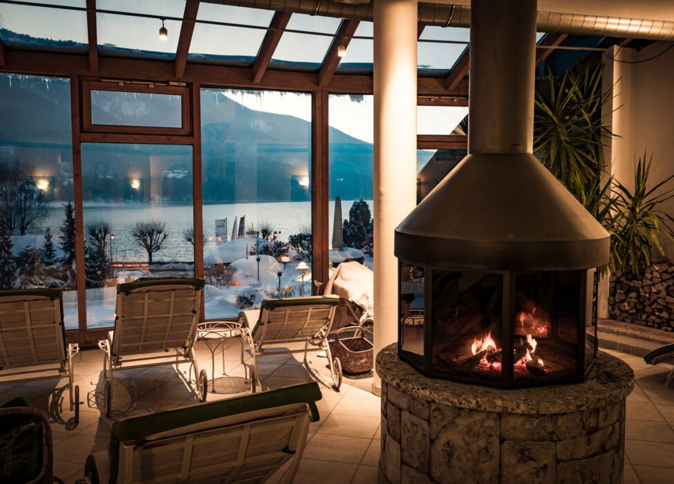 Cozy indoor lounge with a fireplace and scenic snowy lake view through large windows.