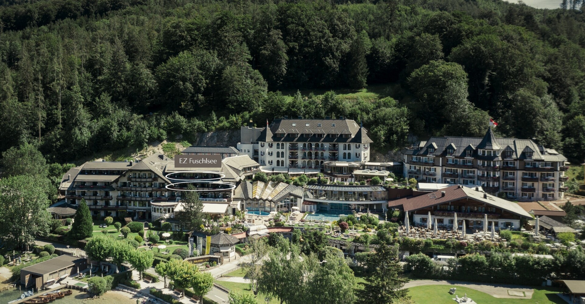 Aerial view of Waldhof Fuschlsee Resort nestled among lush greenery and near a serene lakeside.