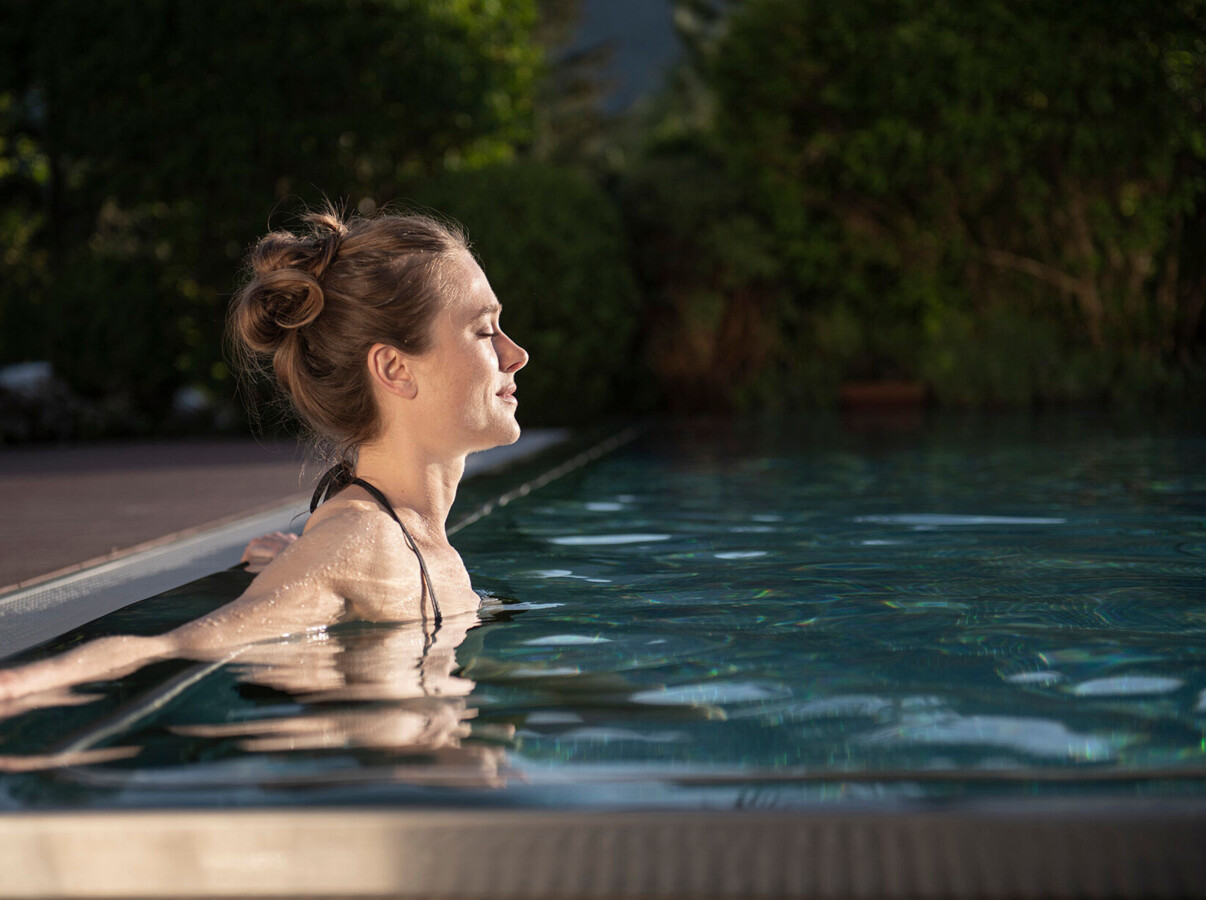 A woman relaxes in a pool surrounded by lush greenery.