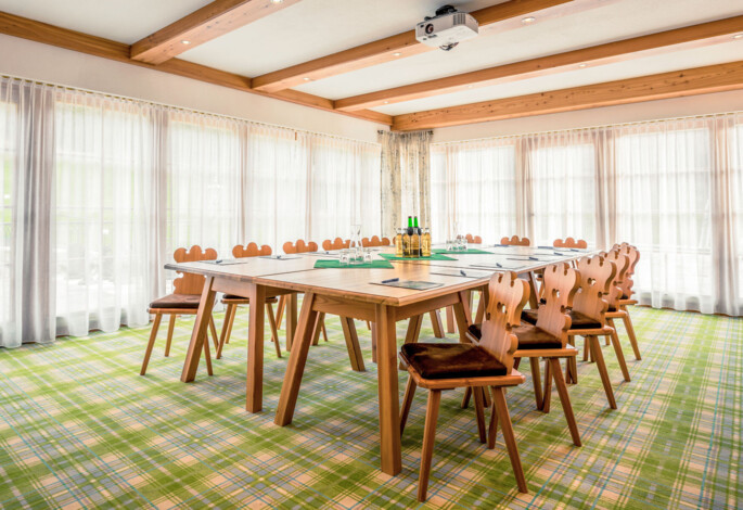 Bright meeting room with wooden chairs around a large table, set on a plaid carpet.