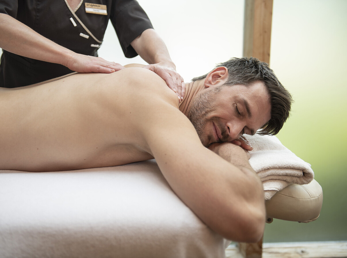 Ein Mann genießt eine entspannende Rückenmassage auf einer Liege, in einem Wellnessbereich.