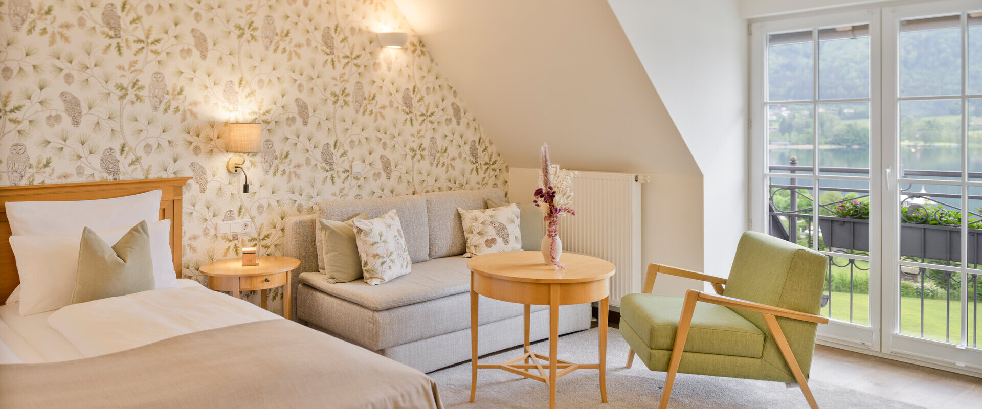 Hotel room with floral wallpaper, cozy seating area, and large windows at Waldhof Fuschlsee Resort.