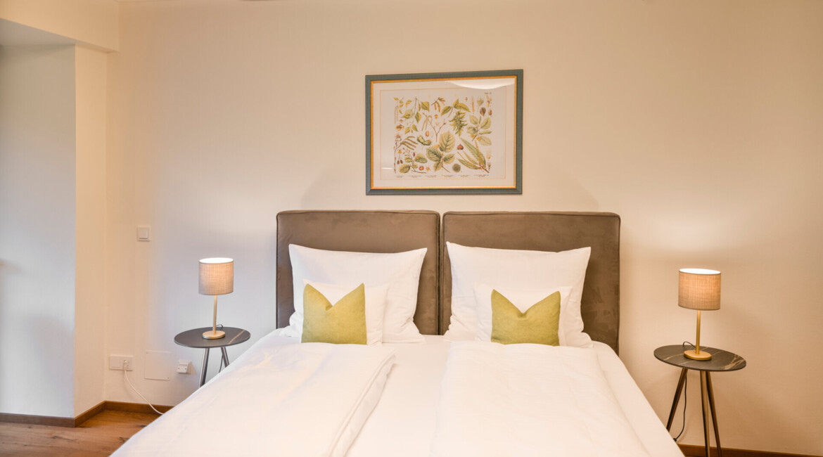 Bedroom with twin beds, green accent pillows, bedside lamps, and nature-themed artwork above the headboard.