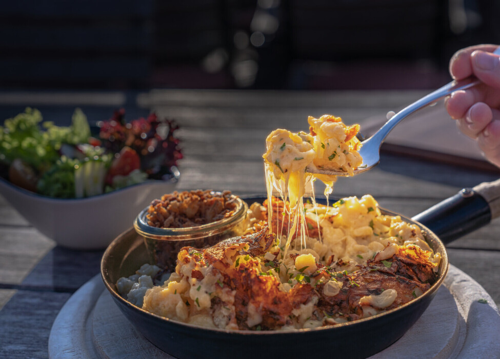 A pan of cheesy pasta with a side salad on a rustic wooden table.