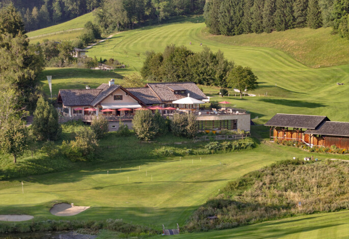 A scenic golf course with a clubhouse surrounded by lush greenery and rolling hills.