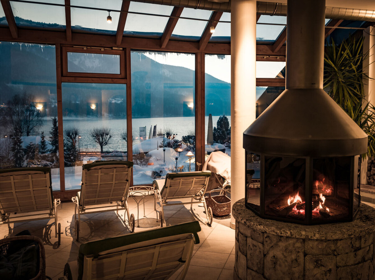 Cozy indoor seating with fireplace, overlooking a snowy lakeside view through large windows.