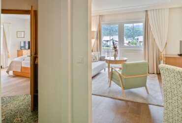 Hotel suite with a bedroom and a living area, featuring elegant furnishings and a scenic view through large windows.