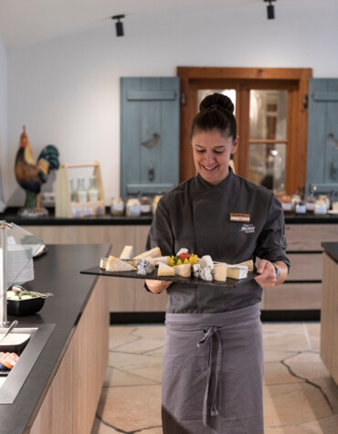 A staff member in a restaurant presents a cheese platter with various cheeses at the breakfast buffet.
