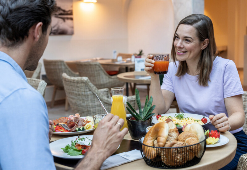 Zwei Personen genießen ein Frühstück mit frischen Säften, Gebäck und Omelett in einem gemütlichen Restaurant.