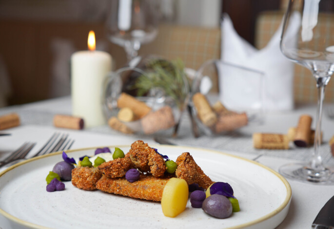 Ein kunstvoll angerichtetes Gourmetgericht auf einem weißen Teller, dekoriert mit bunten Zutaten, auf einem stilvoll gedeckten Tisch mit Kerzenlicht.