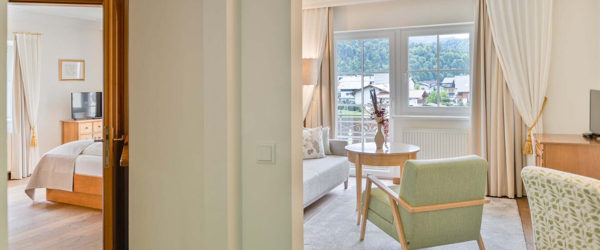 Hotel suite with a bedroom and a living area, featuring elegant furnishings and a scenic view through large windows.