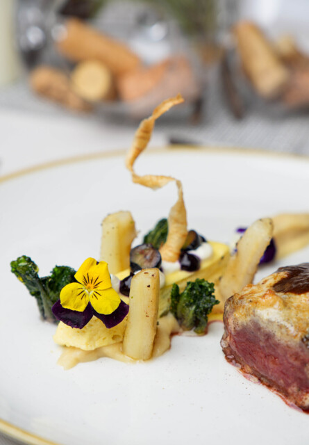 A gourmet dish elegantly plated with vegetables and edible flowers on a white plate.