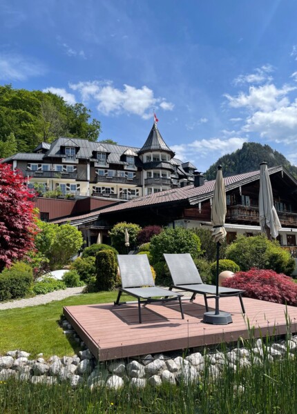 Garten des Waldhof Fuschlsee Resort mit Liegestühlen im Garten, umgeben von üppiger Natur und blauem Himmel.