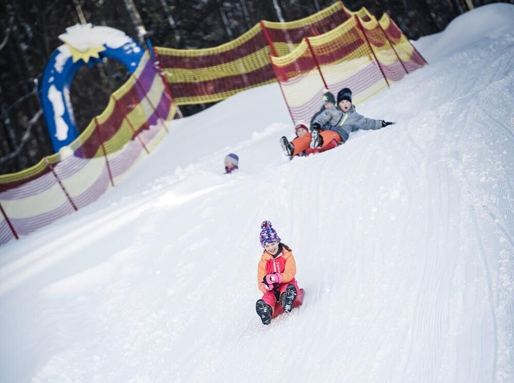 Kinder auf dem Zauberteppich mit Schlitten auf der Waldhofalm - Winterspaß für die ganze Familie.