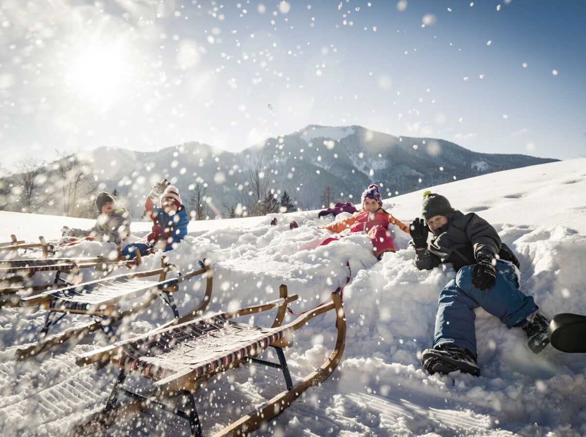 Children playing in snow with sleds on a sunny winter day in the mountains.