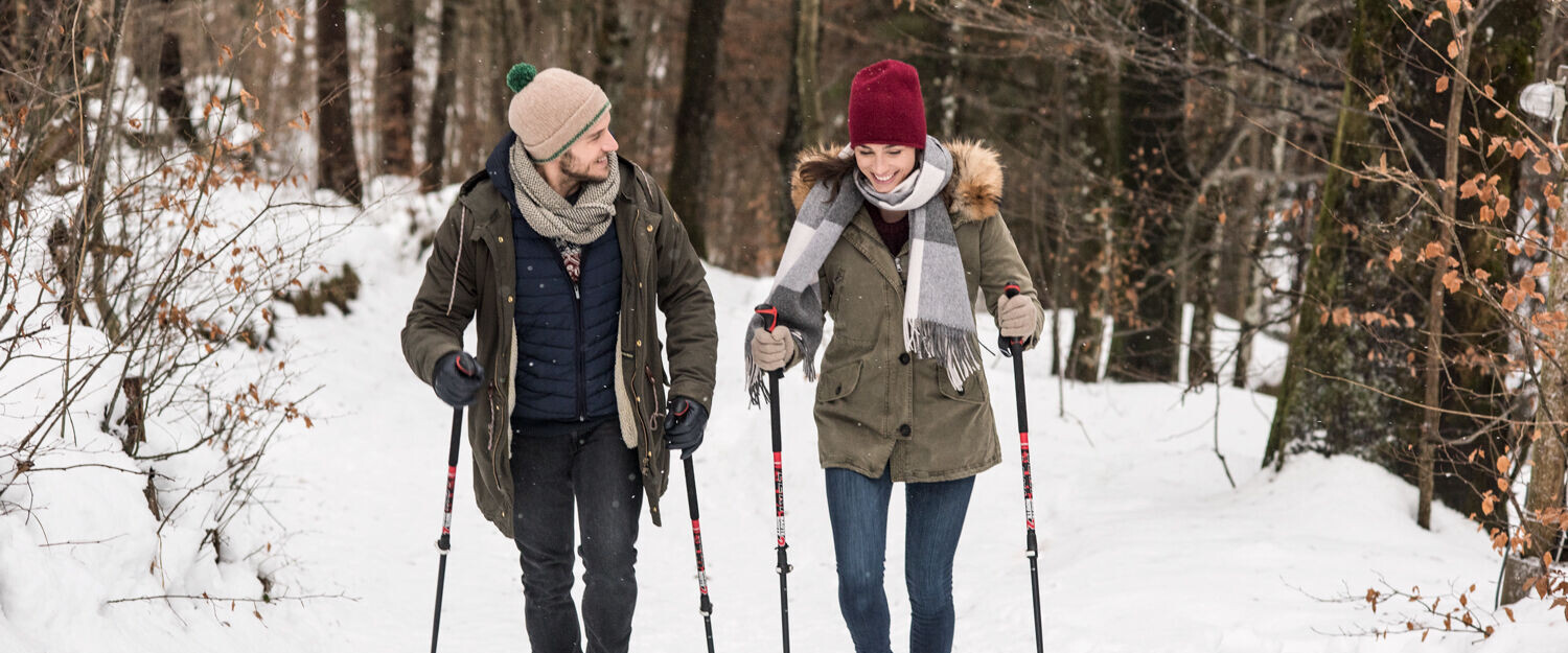 Pärchen beim Winterwandern durch den tief verschneiten Wald am Fuschlsee, Salzburg.