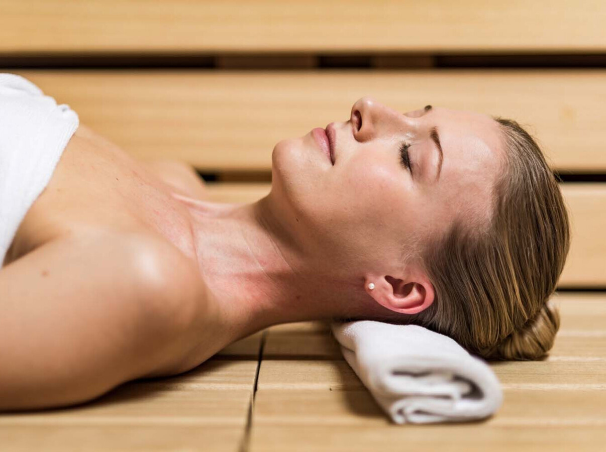 A woman relaxing in a sauna, lying on a towel with eyes closed, enjoying a peaceful moment.