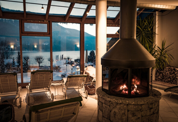 Cozy indoor lounge with a fireplace and scenic snowy lake view through large windows.