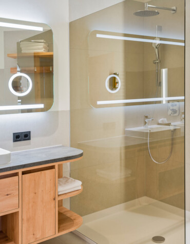 Modern bathroom with a glass shower, wooden cabinetry, and illuminated mirrors.