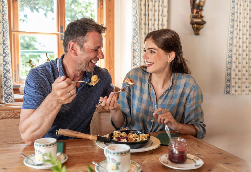 A couple enjoying a meal together at a cozy wooden table with a window view.