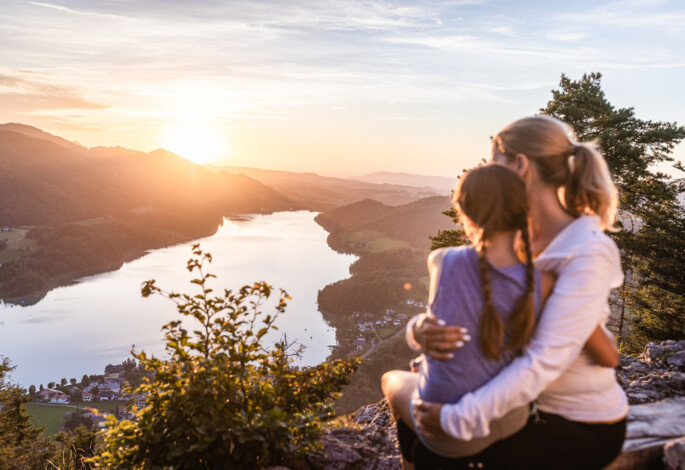 Mutter mit Kind bei einem Gipfelkreuz bei Sonnenuntergang über dem Fuschlsee, Salzkammergut.