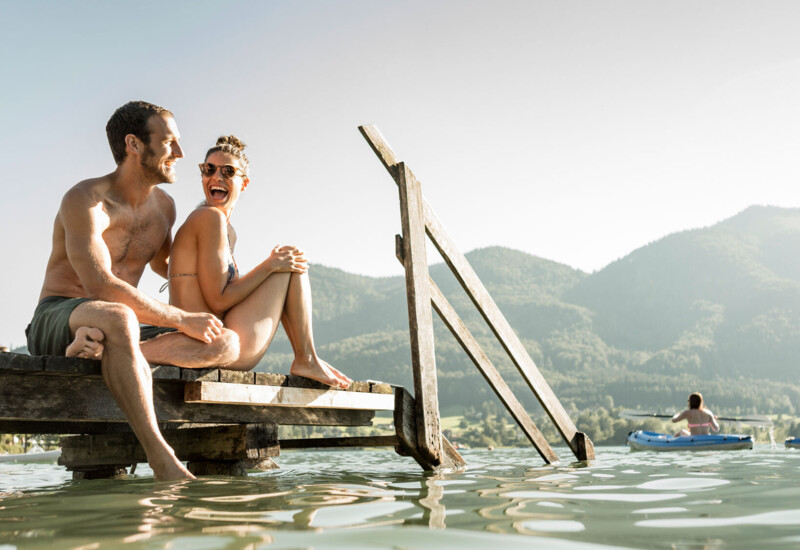 Junges Pärchen sitzend am Badesteg des Wellnesshotel Ebner's Waldhof im Salzburger Land.