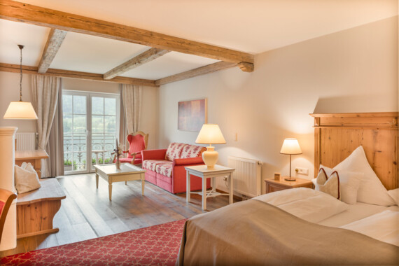 Hotel room with wooden beams, a double bed, red sofa, and balcony doors.