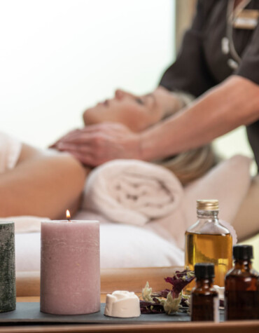 A woman enjoys a relaxing massage with candles and essential oils nearby.