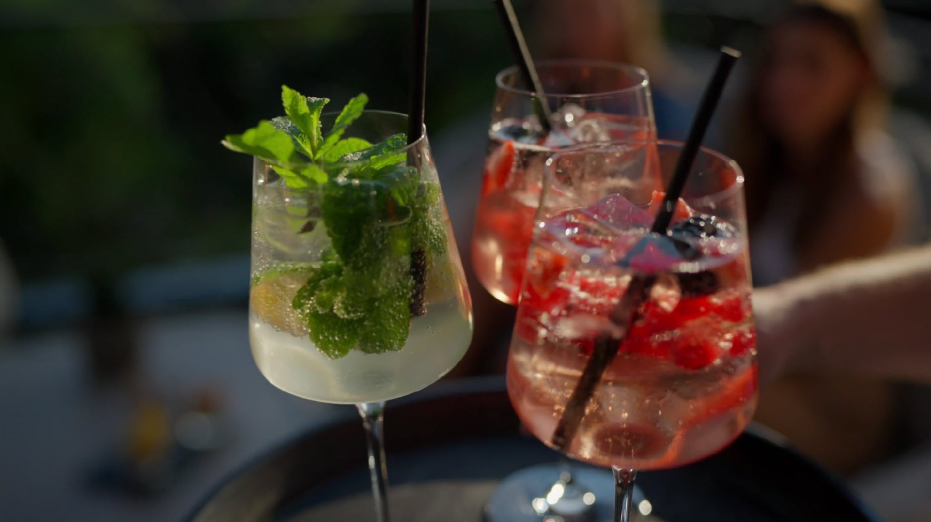 Three refreshing cocktails with mint and berries on a tray.