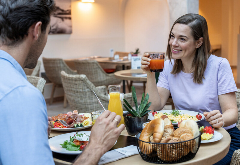 Zwei Personen genießen ein Frühstück mit frischen Säften, Gebäck und Omelett in einem gemütlichen Restaurant.