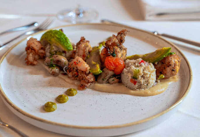 Gourmetgericht mit Garnelen, Couscous und Gemüse kunstvoll auf einem Teller angerichtet.