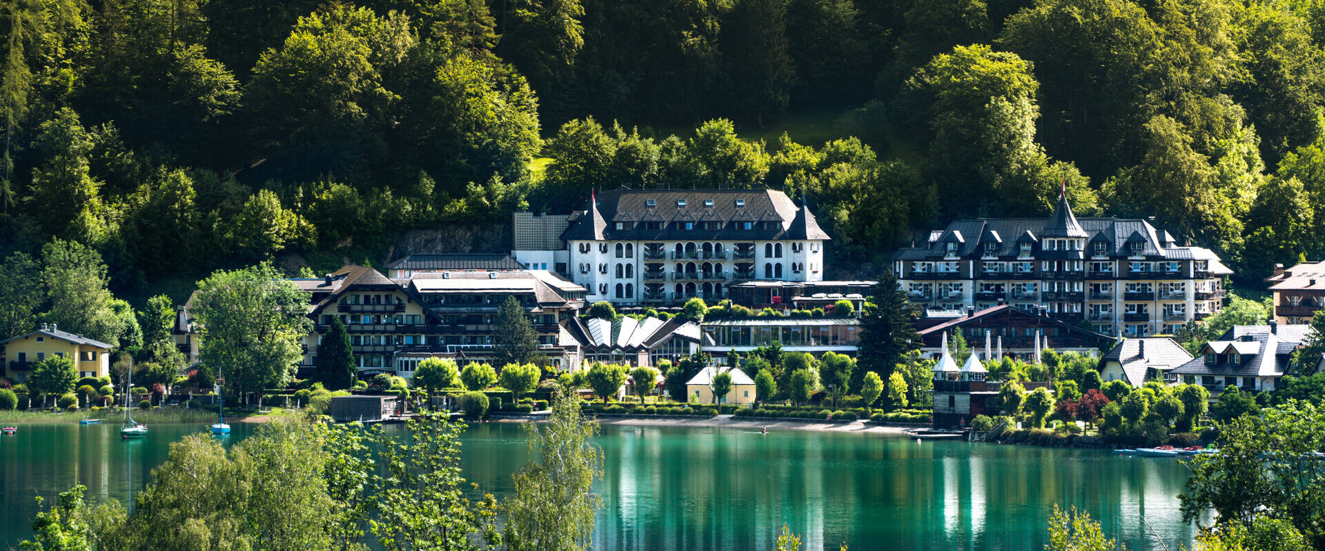 Waldhof Fuschlsee Resort am Ufer des Fuschlsees, umgeben von üppigen Wäldern und reflektiert im klaren Wasser.