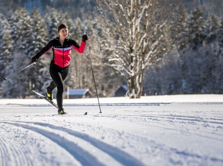 Langläuferin in roter Jacke auf verschneiter Spur, umgeben von winterlicher Waldlandschaft.