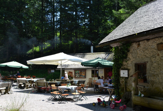 Outdoor seating area with tables and umbrellas at a rustic cafe surrounded by lush forest.