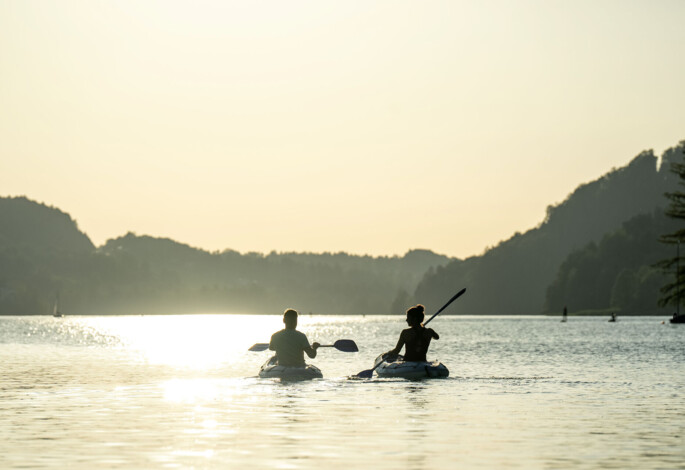 Zwei Personen paddeln im Sonnenuntergang auf dem Fuschlsee.