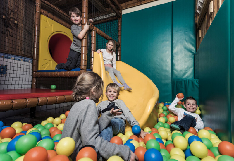 Children playing in a colorful indoor ball pit with a slide, enjoying a fun and playful environment.