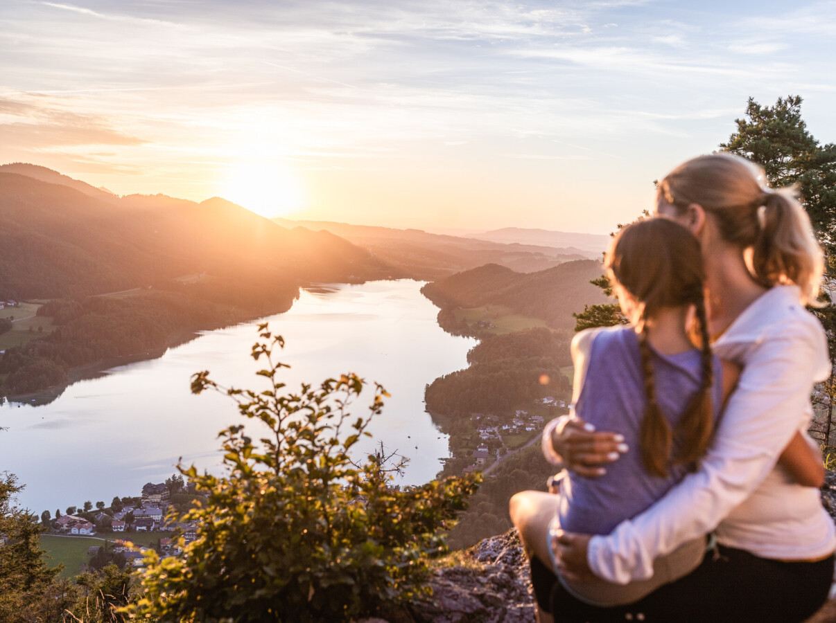 Mutter mit Kind bei einem Gipfelkreuz bei Sonnenuntergang über dem Fuschlsee, Salzkammergut.