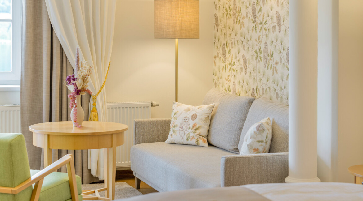 Bright hotel room with a cozy sofa, floral wallpaper, and soft lighting, creating a welcoming atmosphere.