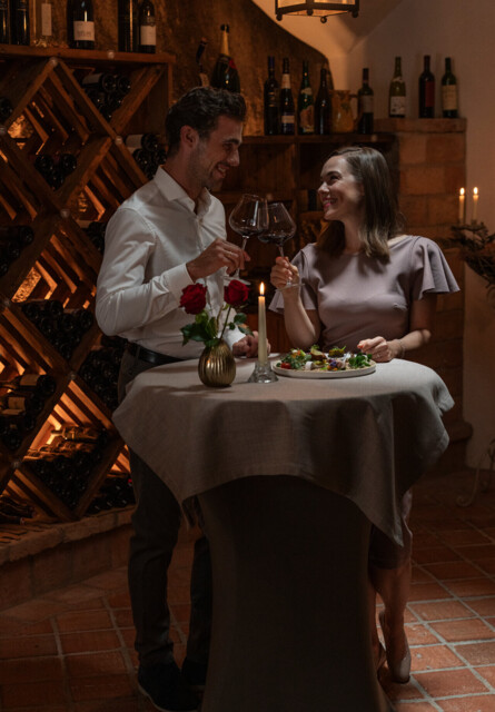 A couple enjoying wine and a candlelit dinner in a cozy wine cellar.