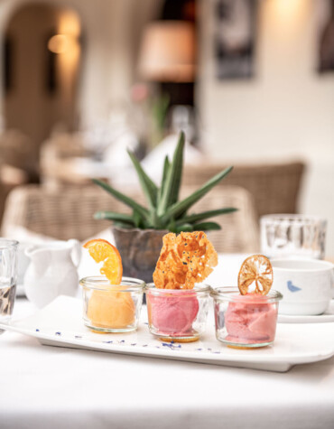 Three sorbet servings in glass jars with decorative citrus slices, displayed on a white plate in an elegant dining setting.