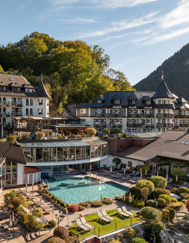 Waldhof Fuschlsee Resort nestled in lush greenery, featuring a scenic outdoor pool and elegant architecture, surrounded by forested hills.
