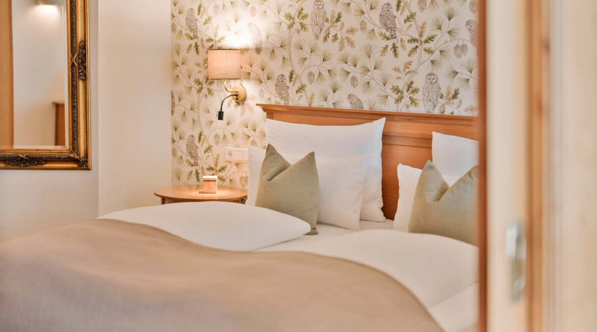 Cozy bedroom with floral wallpaper, soft bedding, and a warm light fixture.