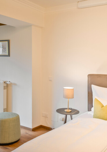 Cozy bedroom with a bed, side table, and lamp, featuring garden views through a large window.