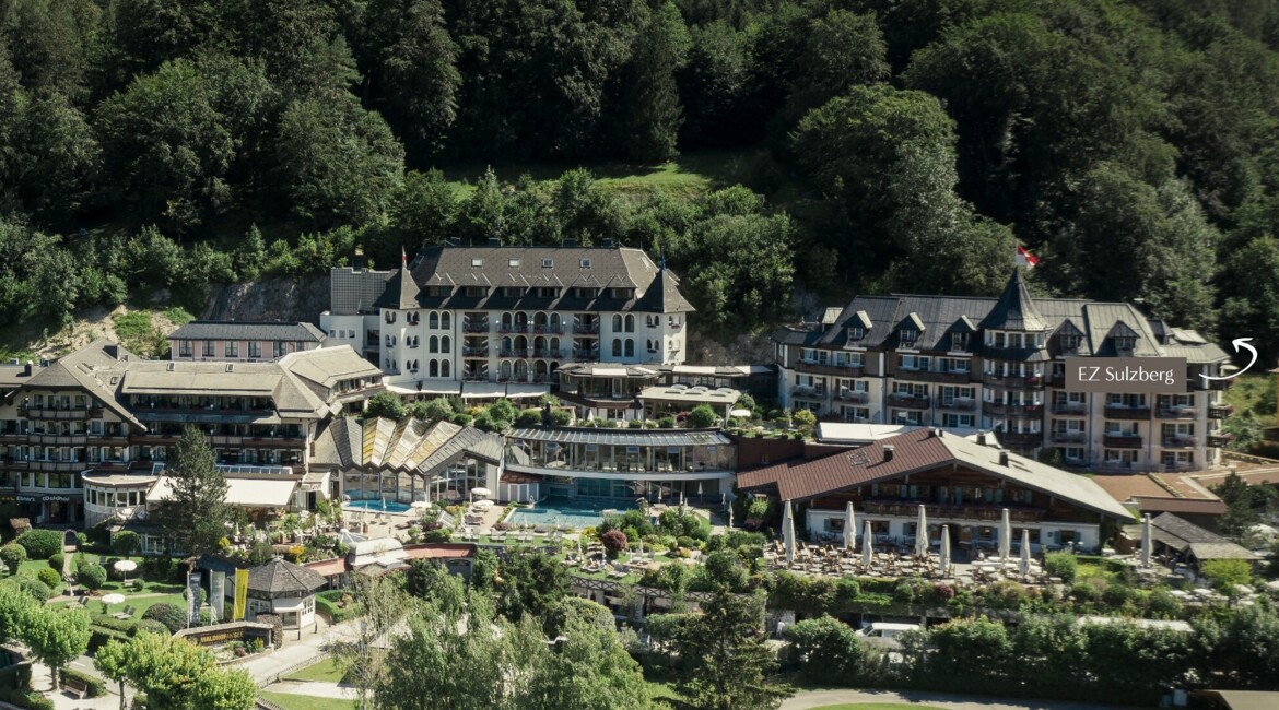 Luftaufnahme vom Waldhof Fuschlsee am Seeufer, umgeben von üppigem Wald, mit gepflegten Gärten und einem Poolbereich.